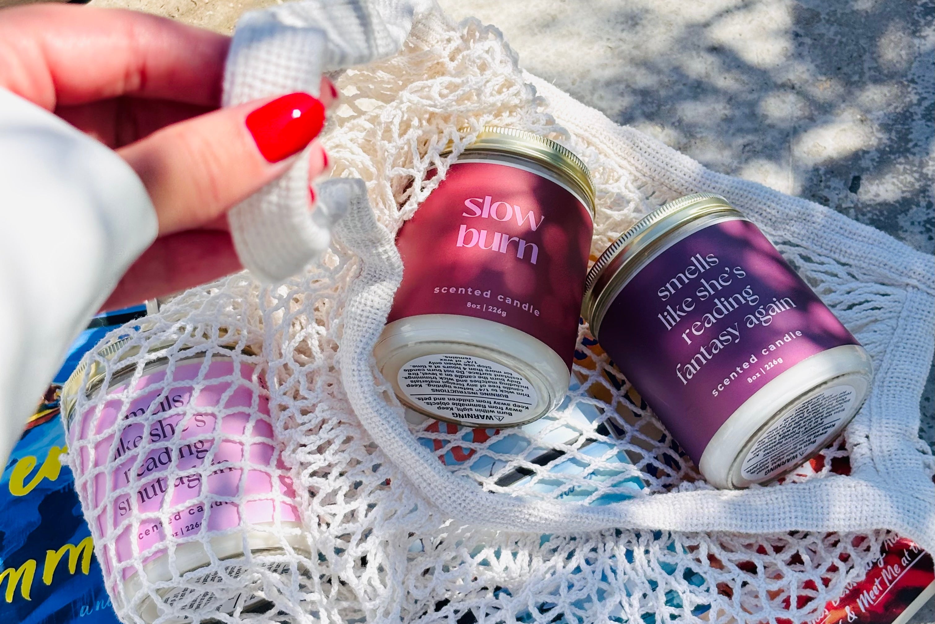 Two scented candles in decorative tins on a textured surface with books underneath.